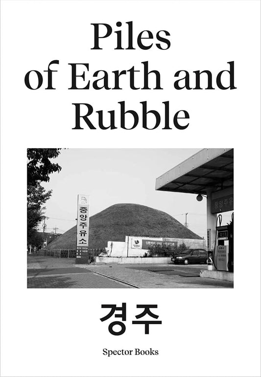 The cover of the book 'Piles of Earth and Rubble' features a black and white photograph of a large pile of rubble, with the title and author's name in white text. The background suggests a cityscape with trees and buildings.