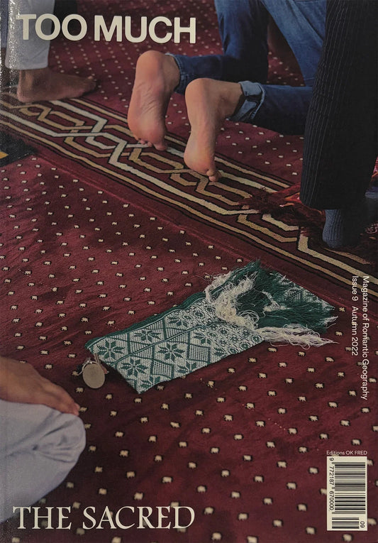 Magazine cover with a patterned rug and feet on a red textured surface, featuring text 'Too Much' and 'The Sacred'.
