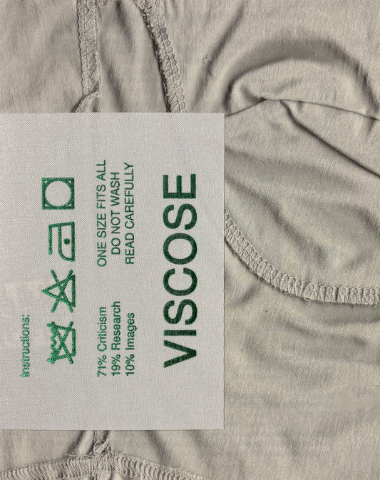 A close-up of a light gray fabric garment showing a sewn-on care label that reads 'VISCOSE' with care instructions and green symbols.